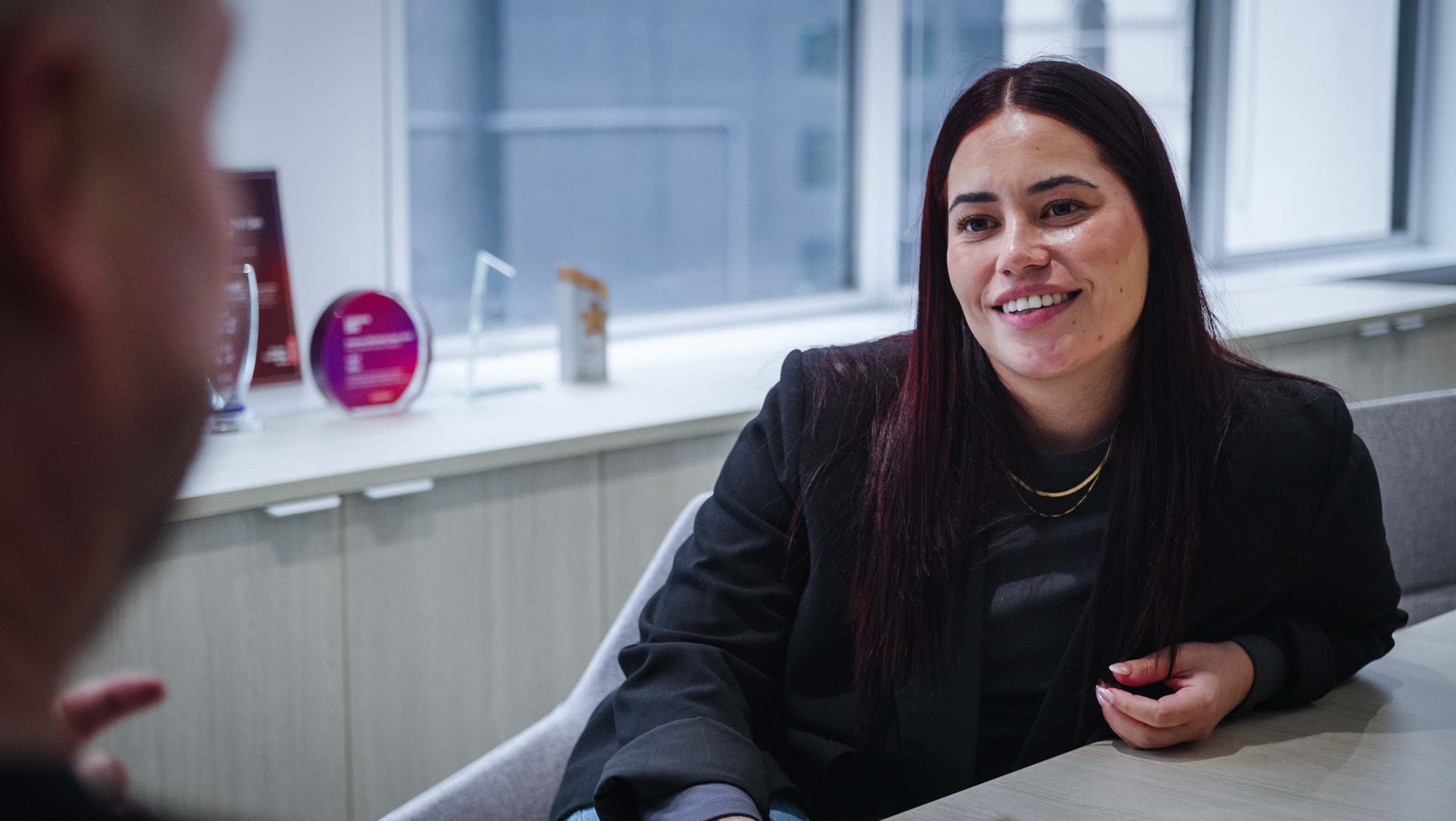 A LAB3 team member smiling during a meeting in a modern office with awards in the background