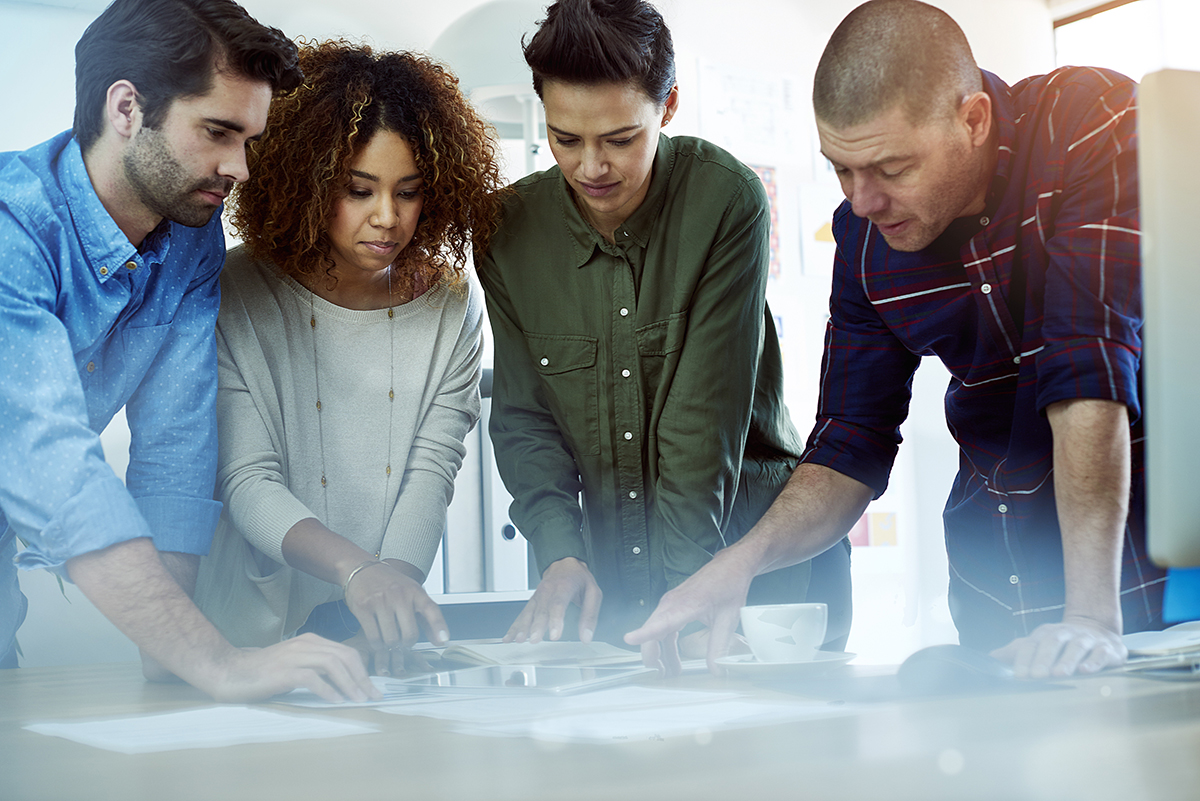 Four colleagues collaborating over documents and tablets in a bright modern office